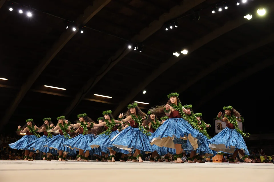 A line of hula dancers turning in flowing blue skirts.