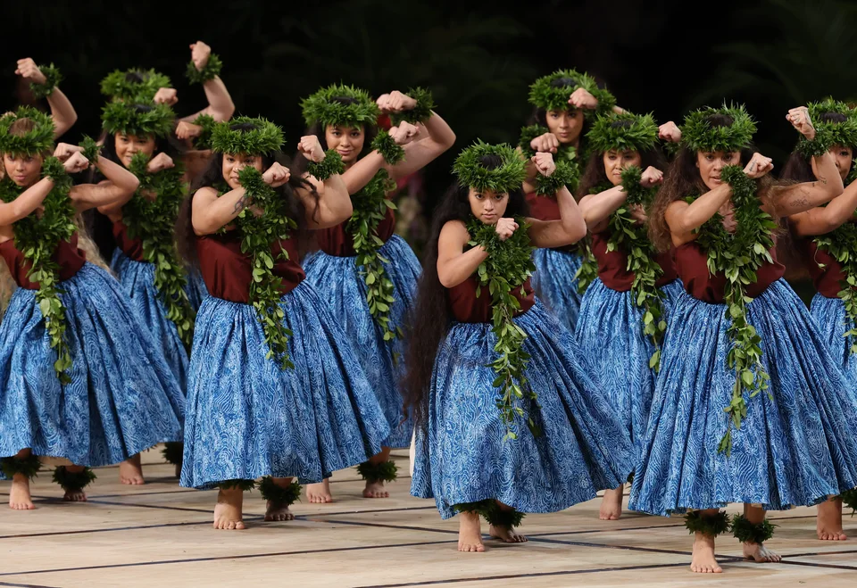 Dancers in blue skirts and green lei sharing a synchronized movement.