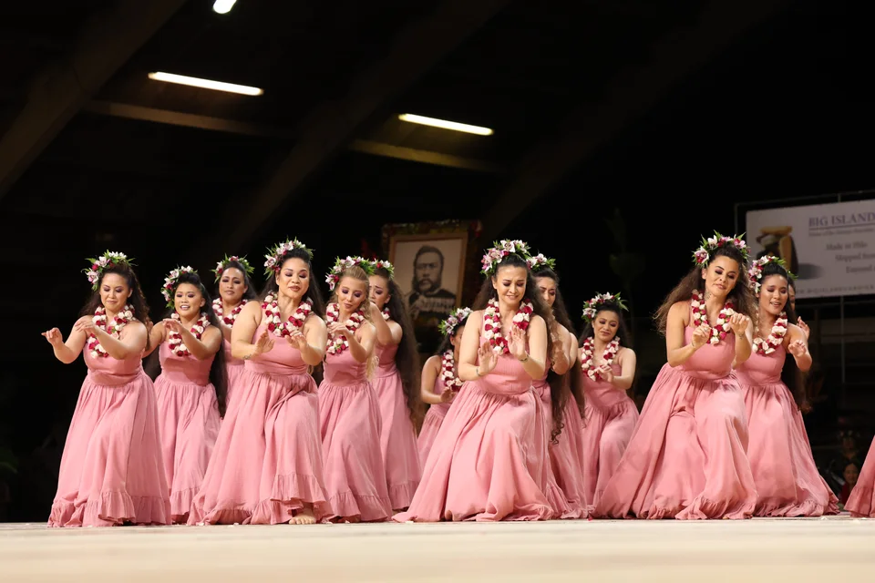 Hālau dancers performing together in pink dresses.